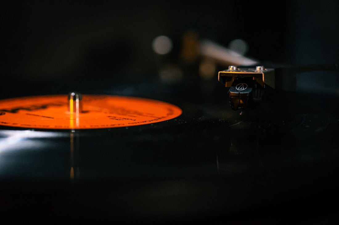 Un vinilo gira en el plato, el brazo apoyado sobre el surco, reflejos naranjas en la penumbra