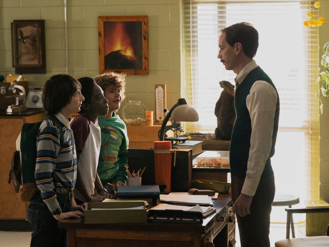 El señor Clarke, con chaleco verde, frente a Mike, Lucas y Dustin en el aula de ciencias.