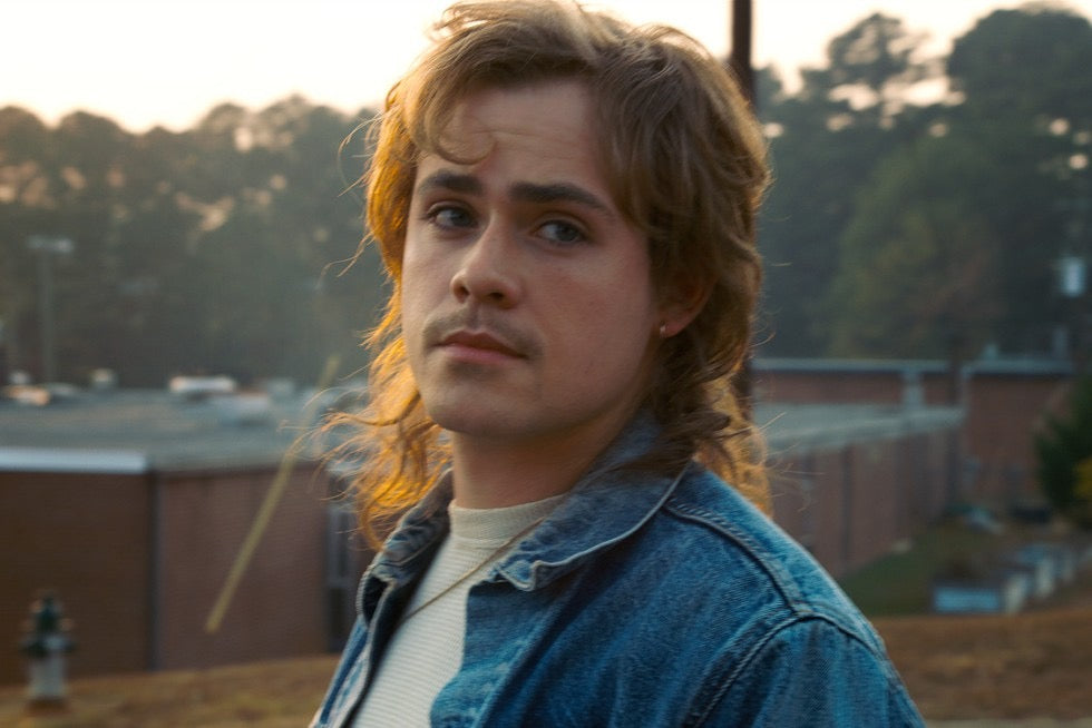 Billy Hargrove, el hermano de Max, con chaqueta vaquera, la mirada hacia un lado