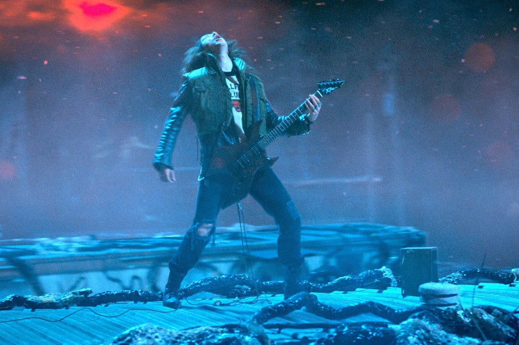 Eddie Munson toca la guitarra Stranger Things, cabeza hacia atrás, en el tejado del Mundo del Revés