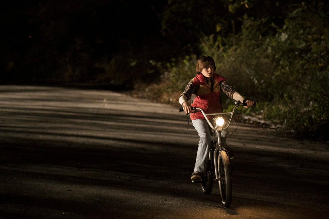 Will en bici, de noche, en una carretera entre árboles, con el faro encendido.